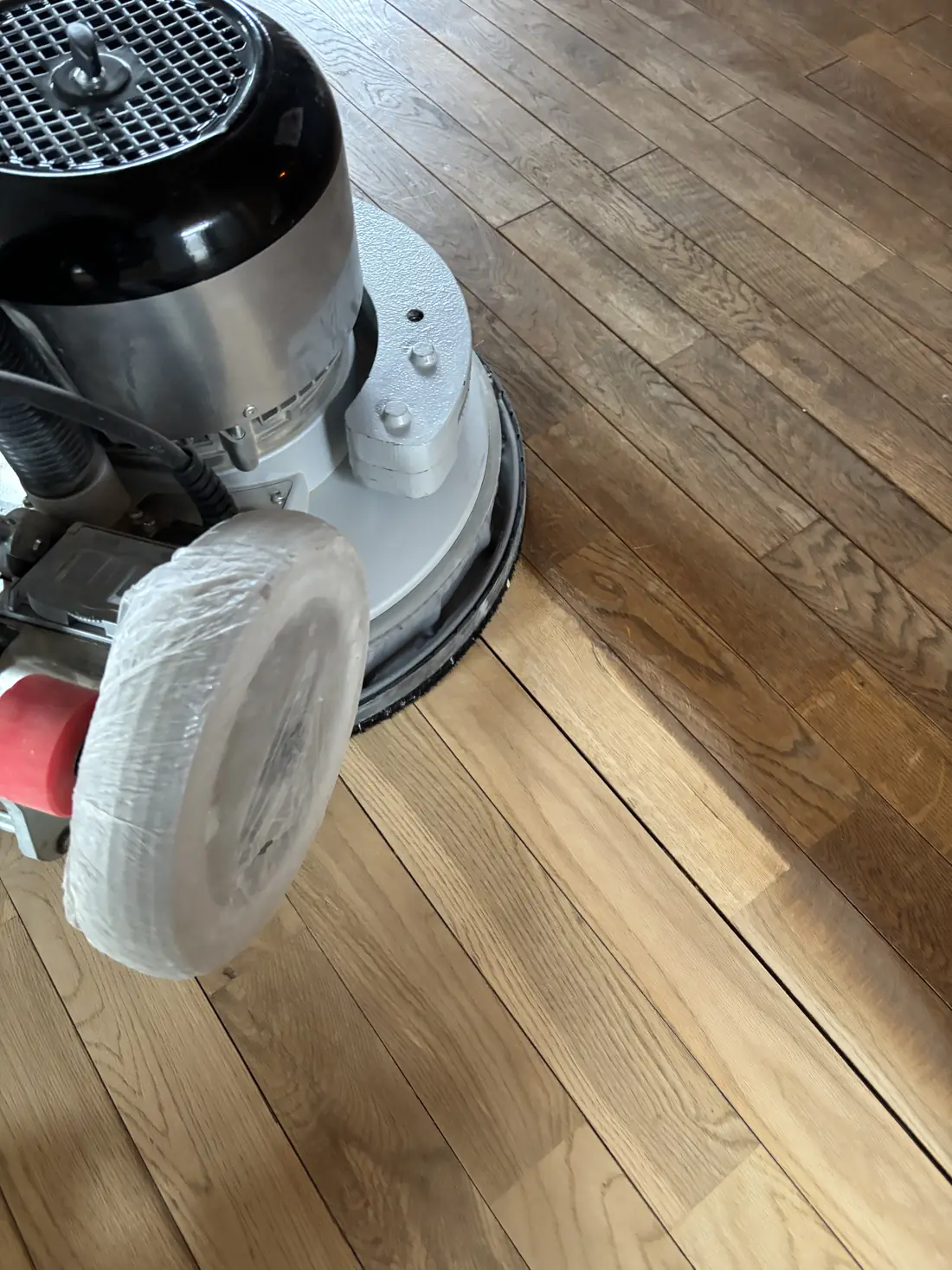 Bonaの研磨機でナラ材のフローリングを削っている様子。境目でシミの有無がはっきり分かれている